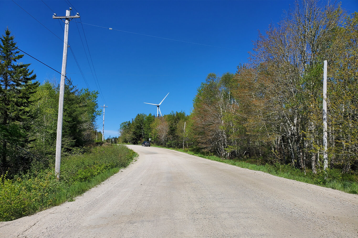 The graded, gravel road leading to the main site, with an on-site wind turbine in the background
